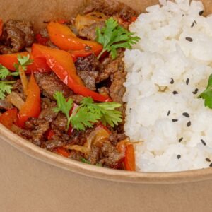 Close-up of a savory beef and vegetables dish with rice in a paper bowl.