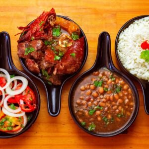 Top view of traditional Brazilian dishes with rice, beans, beef, and fresh salad served in black bowls.